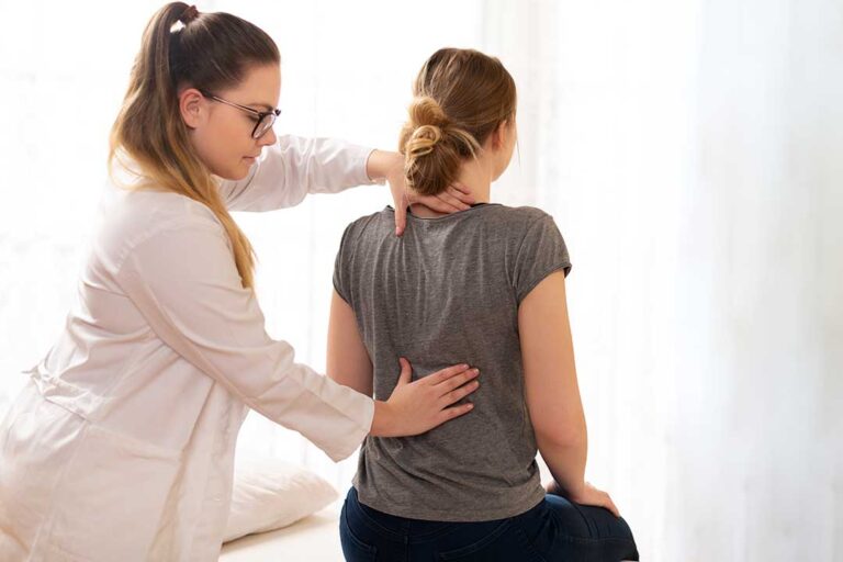 An adult correctly lifting a box in a home setting, demonstrating proper squatting posture with a neutral spine.
