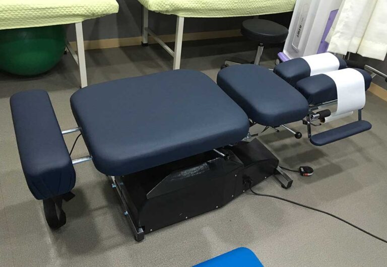Person gently stretching a sore back beside a treatment table in a bright clinical room.